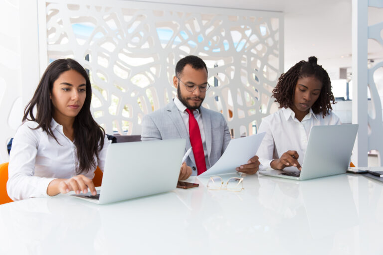 Business professionals checking project data together. Business man and women sitting at conference table, using laptops, reading documents. Working professionals concept